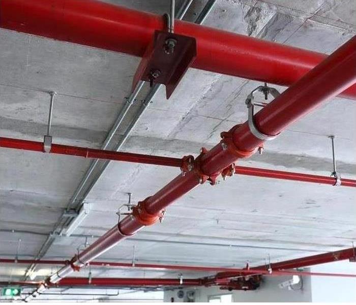 An overhead commercial sprinkler system with red pipes is shown