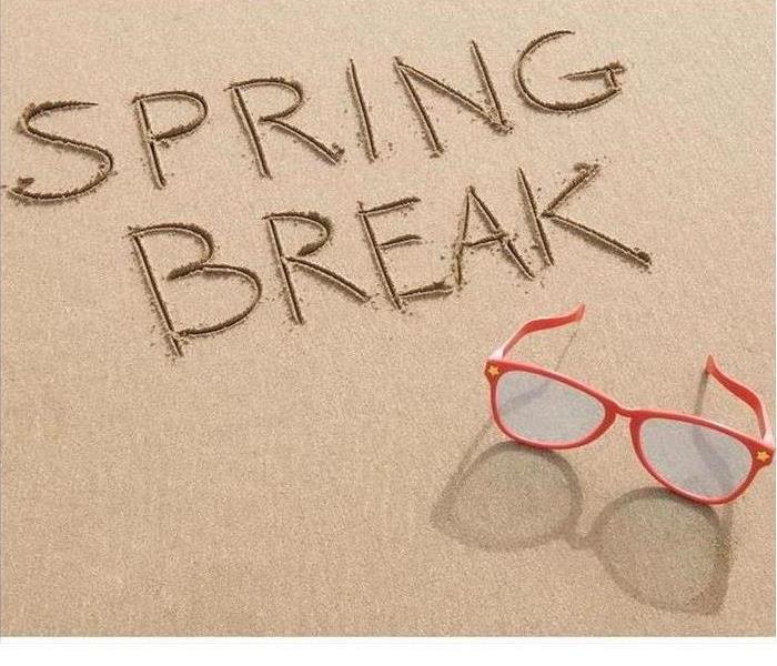 A small patch of sand is shown with the words Spring Break written in the sand and a pair of red sunglasses are nearby