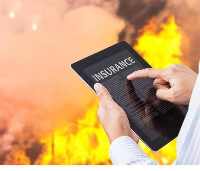 A person's hands are shown holding a tablet looking for insurance information with a fire in the background