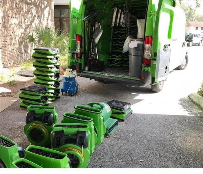 A green SERVPRO van is shown with fans and other equipment unloaded